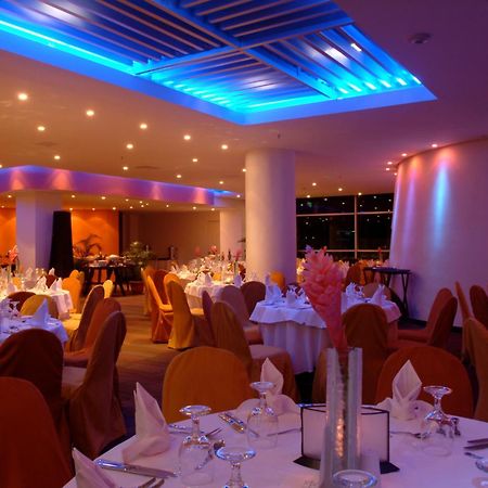 Decapolis Hotel Panama City Facilities photo The image shows an elegant restaurant interior. The dining area features round tables covered with white tablecloths, and each table is set with glassware and napkins. The chairs are draped in orange fabric, contributing to a warm and inviting atmosp
